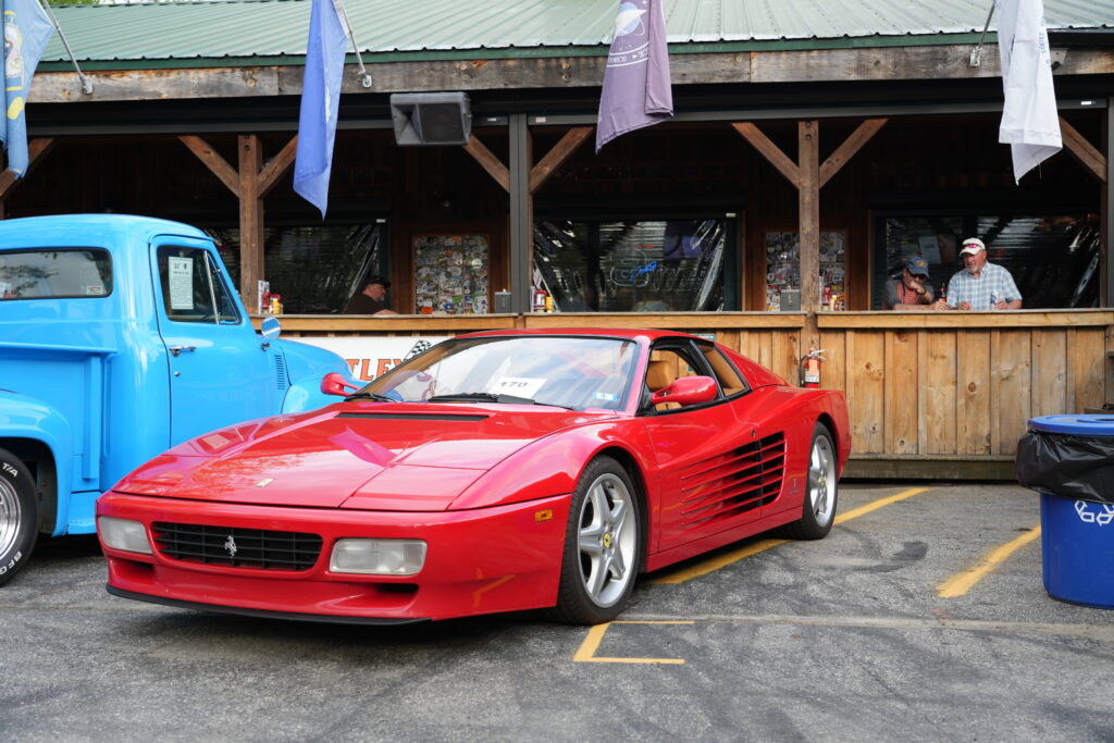 A red Ferrari Testarossa parked beside a vintage blue pickup truck