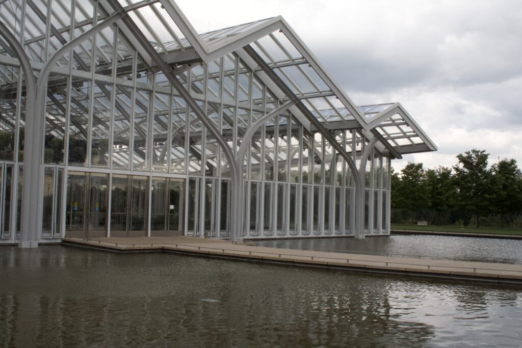 The glass and white steel conservatory reflected in the water beside it