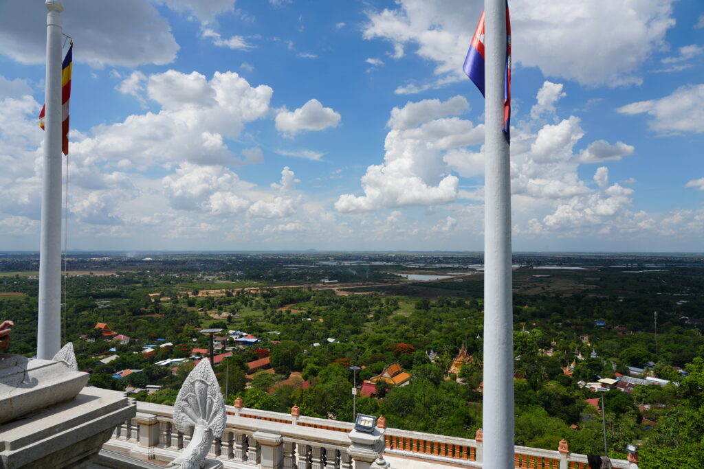 Buddhist and Cambodian flags above a hilltop view of the plain