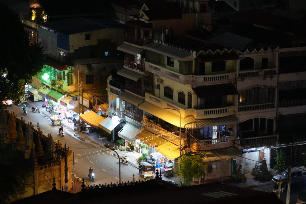 A lit street of shopfronts and awnings seen from above at night