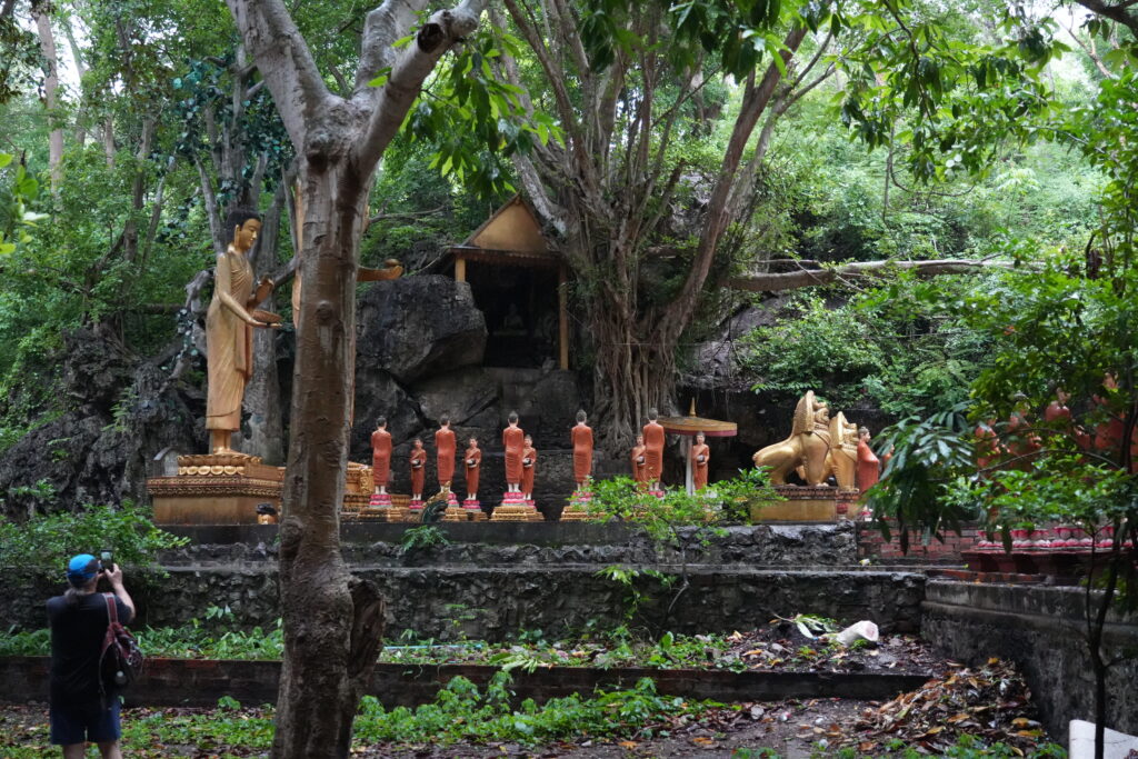 Gold and red statues in a rock shrine beneath dense trees