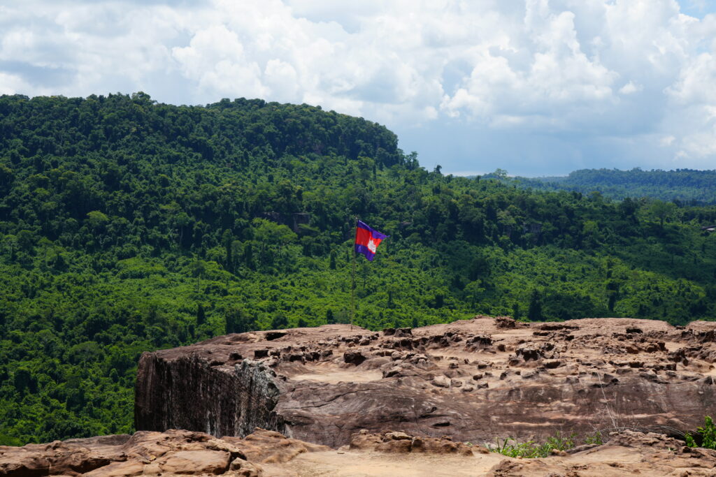 A Cambodian flag on a rock ledge above unbroken green jungle