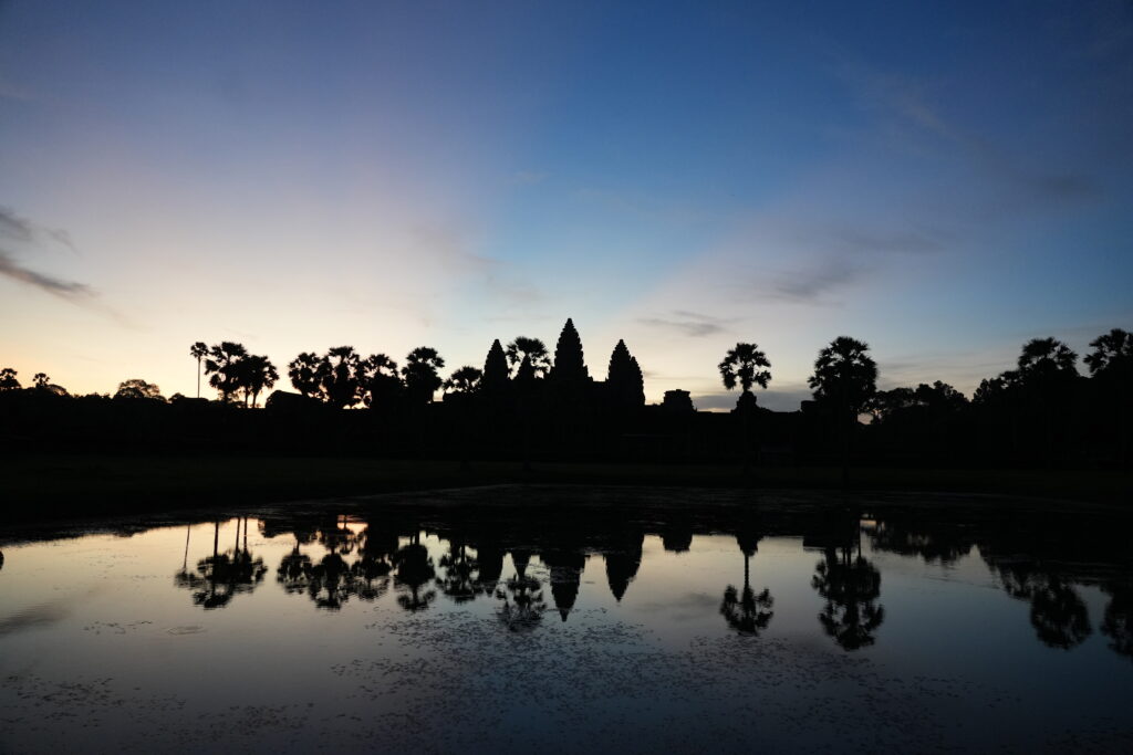 Angkor Wat silhouetted against deep blue dawn and mirrored in water