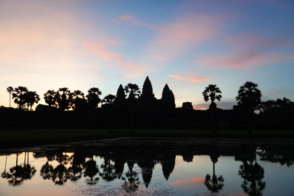 Angkor Wat and sugar palms mirrored under a pink and violet sky