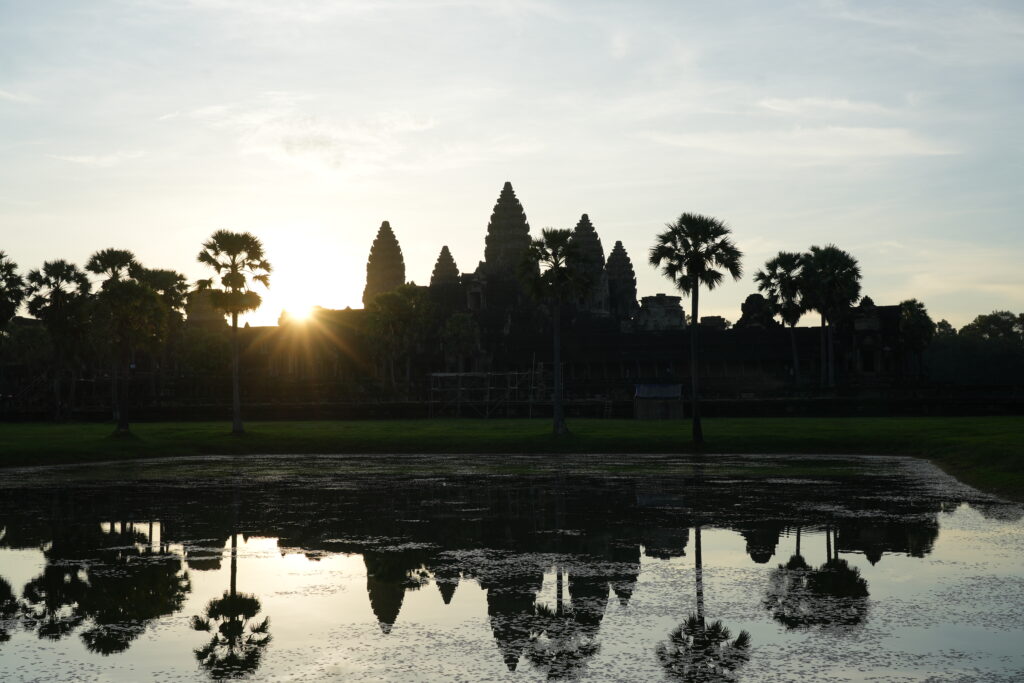 The sun breaking in a starburst beside Angkor Wat, reflected in still water