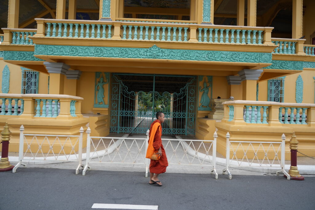 Orange-robed monk passing ornate temple gate