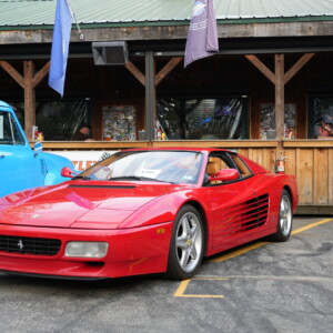 A red Ferrari Testarossa parked beside a vintage blue pickup truck