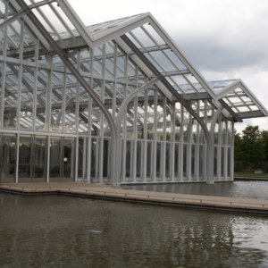 The glass and white steel conservatory reflected in the water beside it
