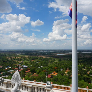 Buddhist and Cambodian flags above a hilltop view of the plain