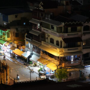 A lit street of shopfronts and awnings seen from above at night