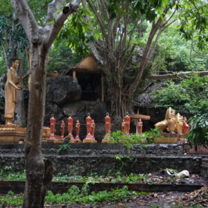Gold and red statues in a rock shrine beneath dense trees