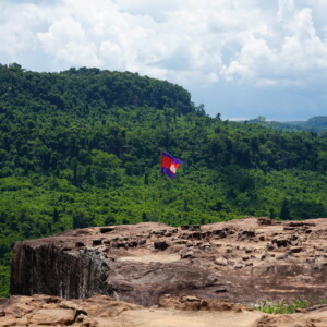 A Cambodian flag on a rock ledge above unbroken green jungle