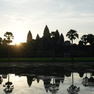 The sun breaking in a starburst beside Angkor Wat, reflected in still water